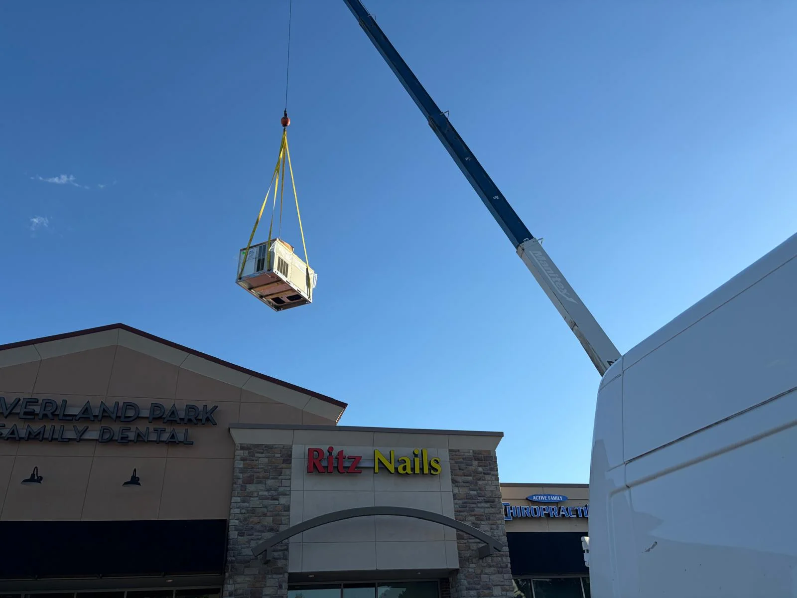 Crane hoisting commercial HVAC unit over Overland Park retail center